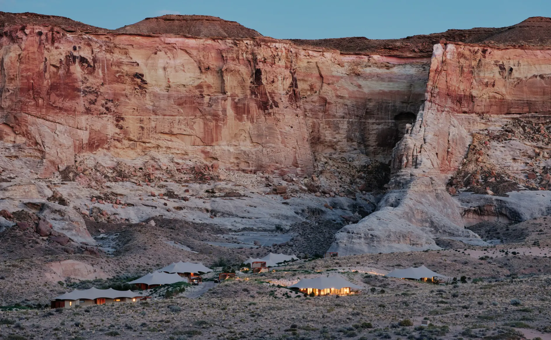 Camp Sarika by Amangiri at dusk — tented pavilions lit beneath a sandstone escarpment in southern Utah